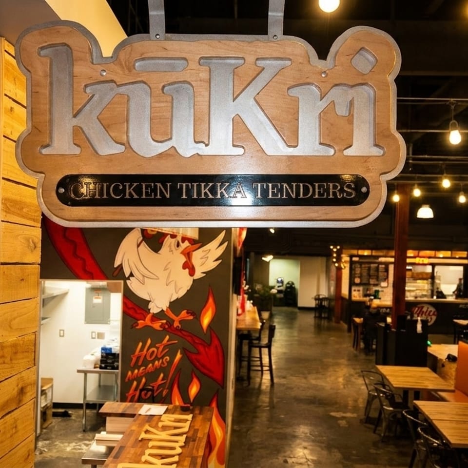 Kukri Chicken Tikka Tenders sign hanging above the entrance to a restaurant with tables and booths.